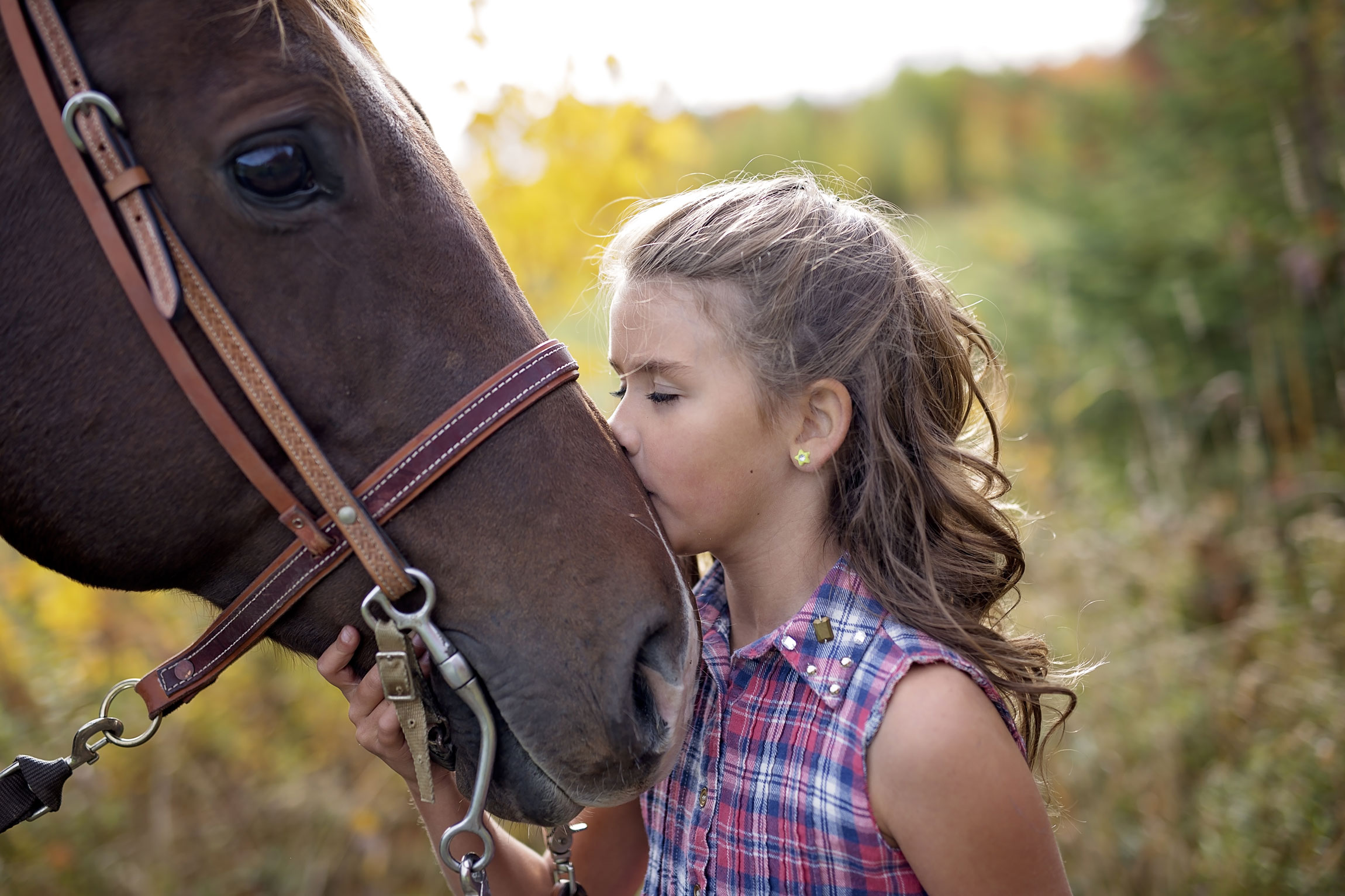 A young girl resting her face against a horse's muzzle in a green field