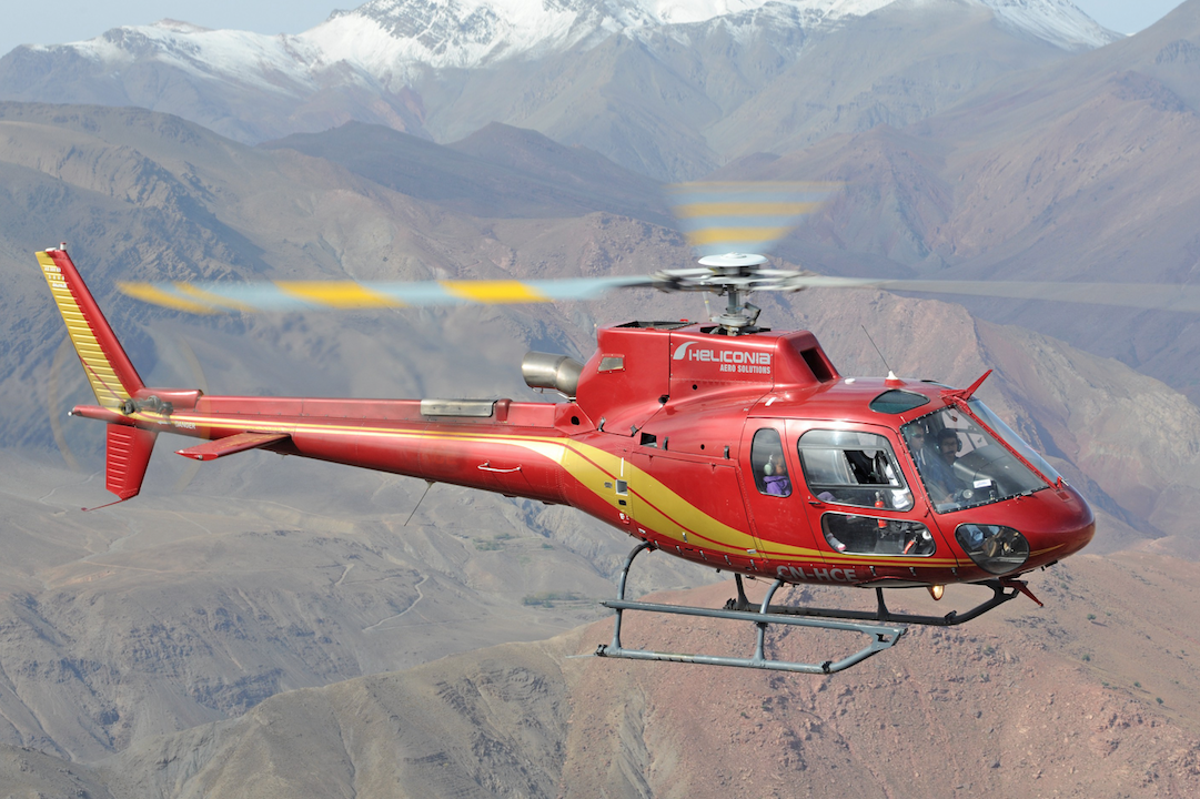 A red helicopter in flight in front of the snow-capped High Atlas