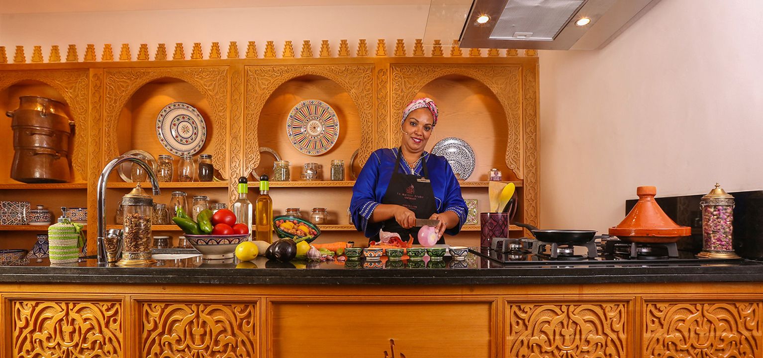 A chef preparing Moroccan dishes in a tiled kitchen with tagines on the counter