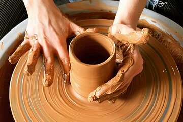 Close view of wet clay rising on the wheel between two hands