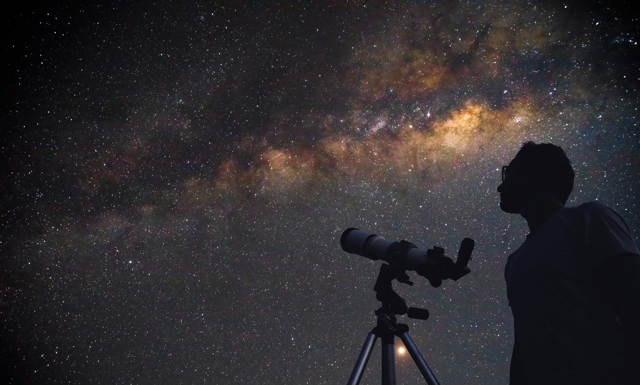 A person beside a telescope under the Milky Way in a dark desert sky