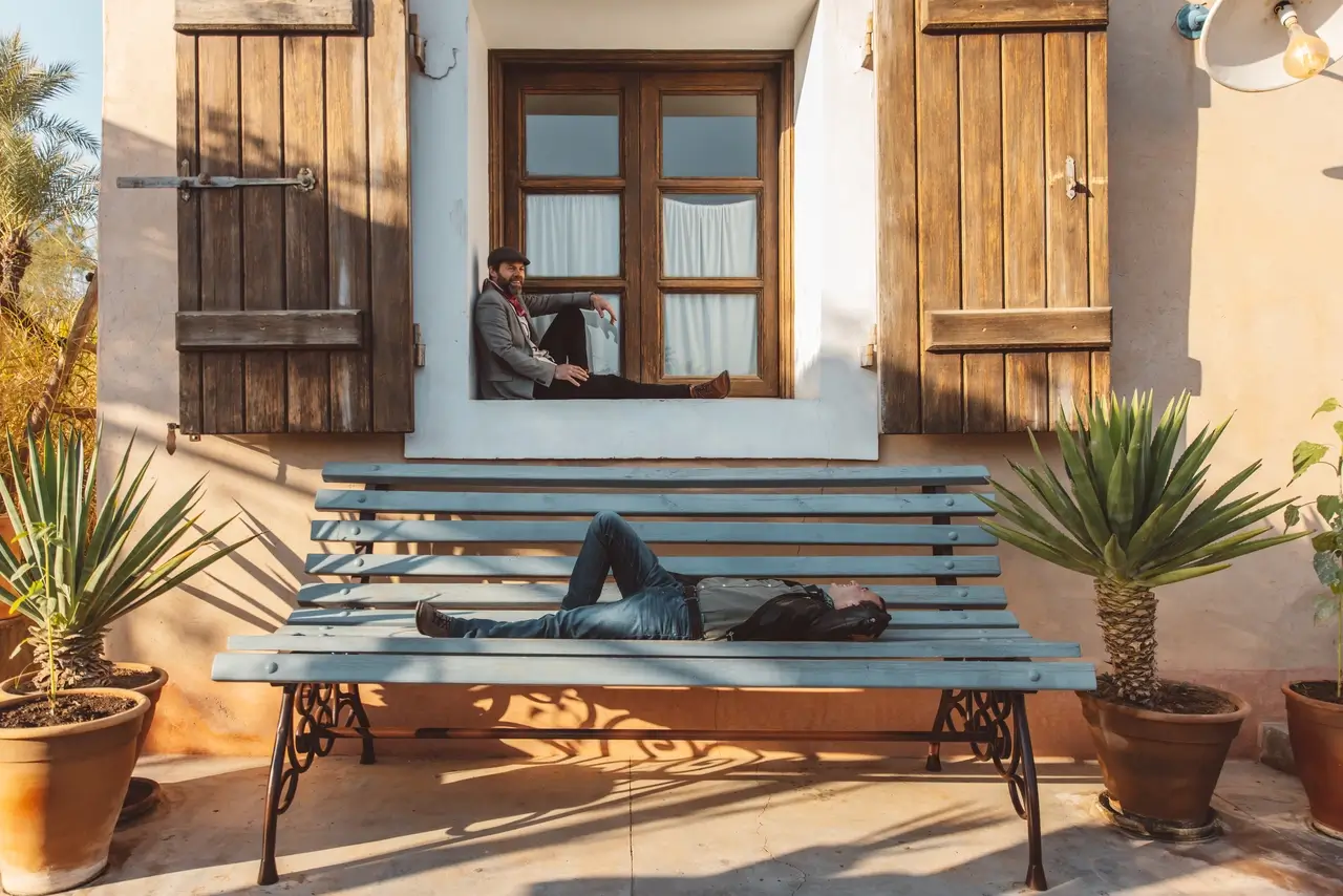 A visitor lying on a giant blue bench in front of an oversized window at the Giant House