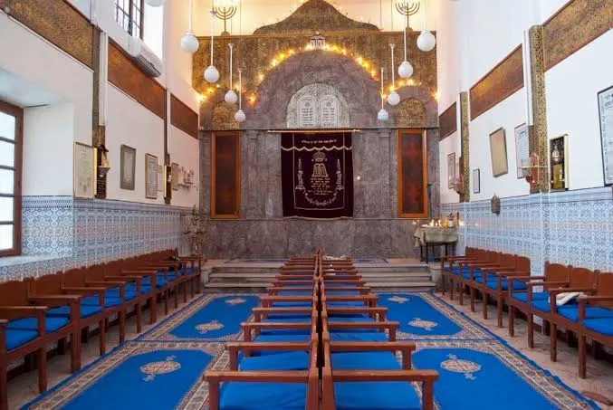 Prayer hall of a restored Moroccan synagogue, with wooden benches and the Torah ark