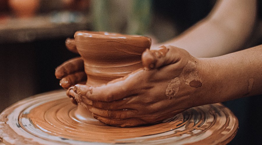 Hands shaping a clay pot on a turning potter's wheel